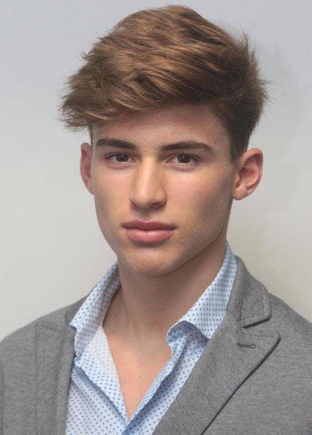 Ein junger Mann mit braunen Haaren und einem grauen Sakko blickt in die Kamera.