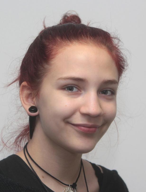 Eine junge Frau mit roten Haaren und Ohrschmuck lächelt.