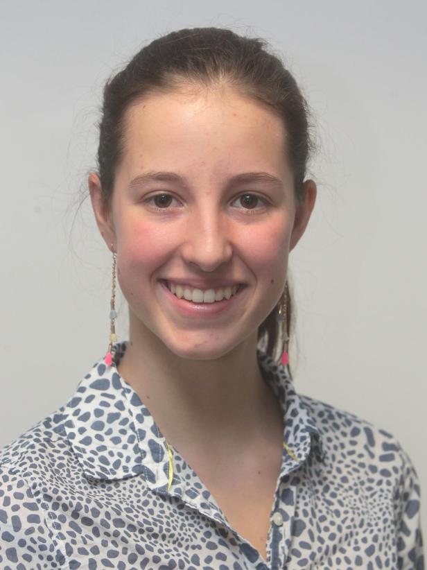 Eine lächelnde junge Frau mit Ohrringen und einem gemusterten Hemd.