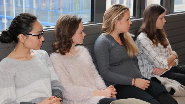 Vier junge Frauen sitzen nebeneinander auf einer Bank und schauen in die gleiche Richtung.