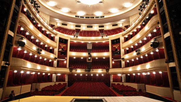 Blick auf den leeren Zuschauerraum eines Theaters mit roten Sitzen und goldenen Verzierungen.