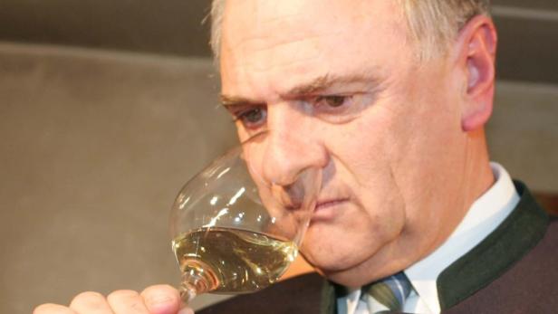 Ein Mann im Anzug riecht an einem Glas Weißwein.