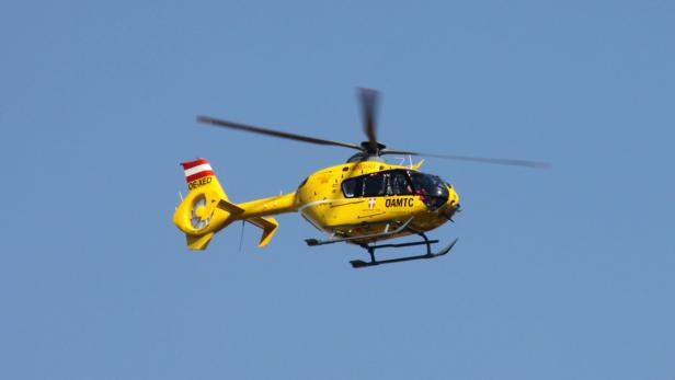 Ein gelber Rettungshubschrauber des ÖAMTC fliegt vor blauem Himmel.