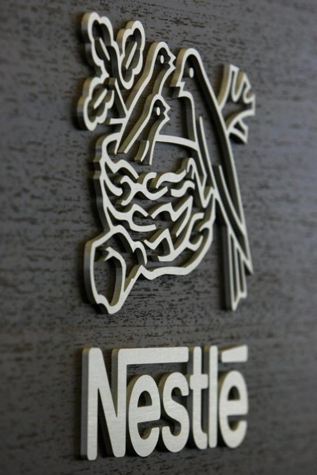 Das Nestlé-Logo mit einem Vogelnest und drei Vögeln auf einer dunklen Holzoberfläche.