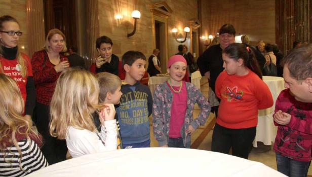 Eine Gruppe von Kindern und Erwachsenen steht um einen Tisch in einem Saal.