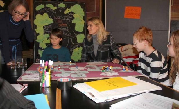 Kinder und Erwachsene sitzen an einem Tisch und spielen mit Legofiguren auf einem Spielbrett.