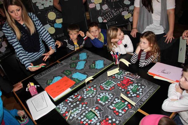 Kinder und Erwachsene betrachten und diskutieren Pläne auf Tischen.