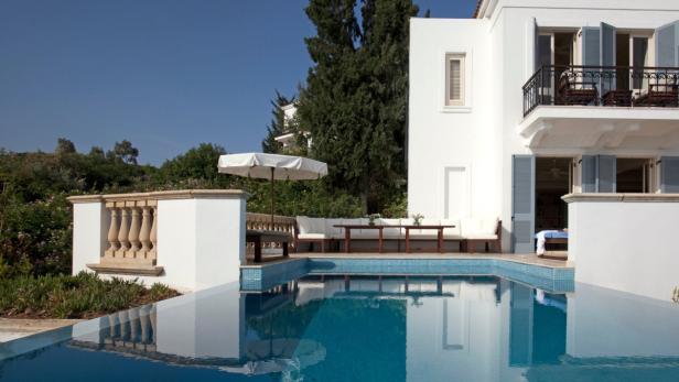 Ein Swimmingpool spiegelt das weiße Gebäude und den blauen Himmel wider.