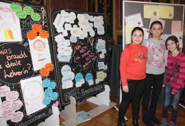 Drei Mädchen stehen vor Tafeln mit Zeichnungen und Texten zum Thema „Was braucht die ideale Lehrerin?“.