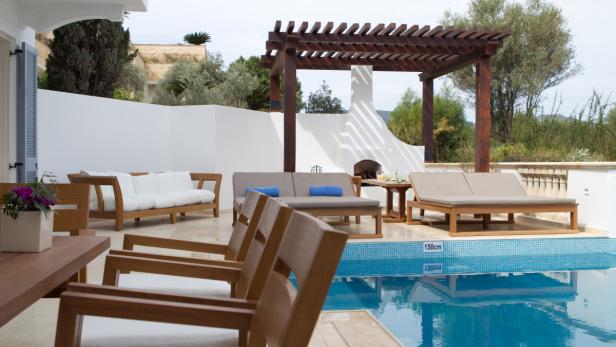 Eine Terrasse mit Gartenmöbeln und einem Pool an einem sonnigen Tag.