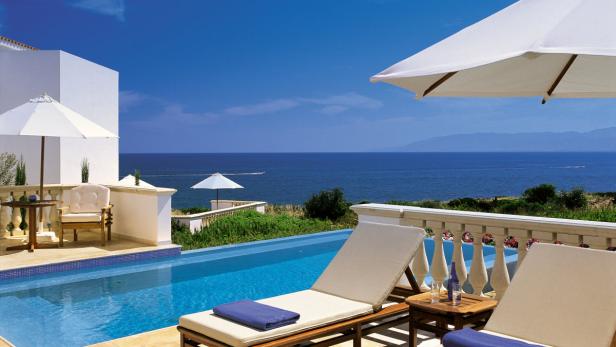 Ein Swimmingpool mit Liegestühlen und Blick auf das Meer an einem sonnigen Tag.