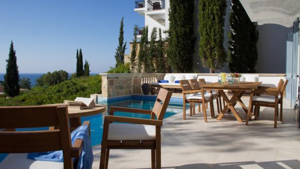 Eine Terrasse mit Holztischen und Stühlen neben einem Pool mit Blick auf das Meer.