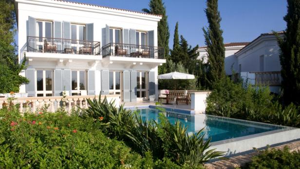 Ein zweistöckiges, weißes Haus mit einem Pool und üppiger Vegetation im Vordergrund.