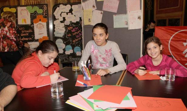 Drei Mädchen sitzen an einem Tisch und basteln mit Papier und Stiften.