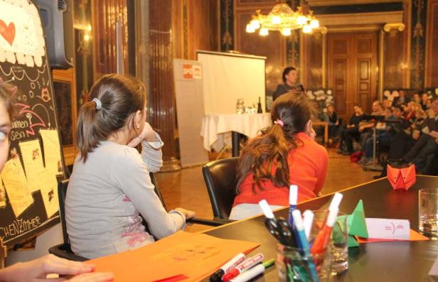 Zwei Mädchen sitzen bei einer Veranstaltung und basteln mit Papier und Stiften.