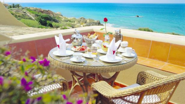 Ein gedeckter Frühstückstisch auf einer Terrasse mit Blick auf das Meer.