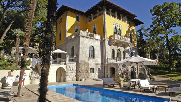 Ein gelbes, mehrstöckiges Gebäude mit einem Swimmingpool im Vordergrund.