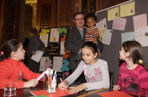 Mädchen sitzen an einem Tisch und basteln, während ein Mann ein Kind im Arm hält.