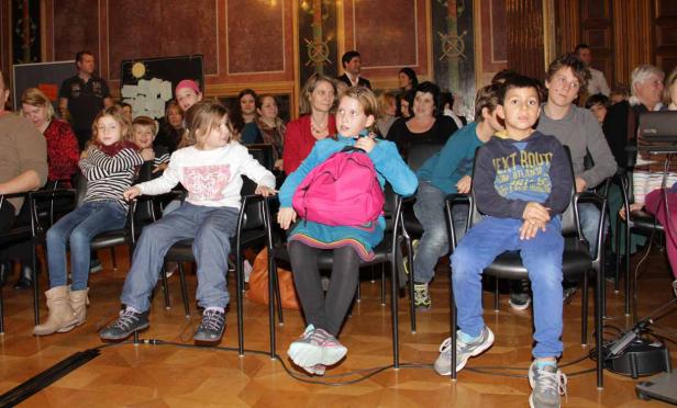 Eine Gruppe von Kindern und Erwachsenen sitzt auf Stühlen in einem Raum.
