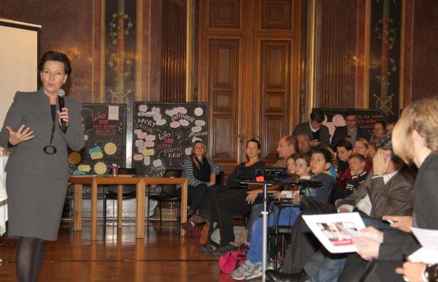 Eine Frau hält eine Präsentation vor einem Publikum in einem Saal.
