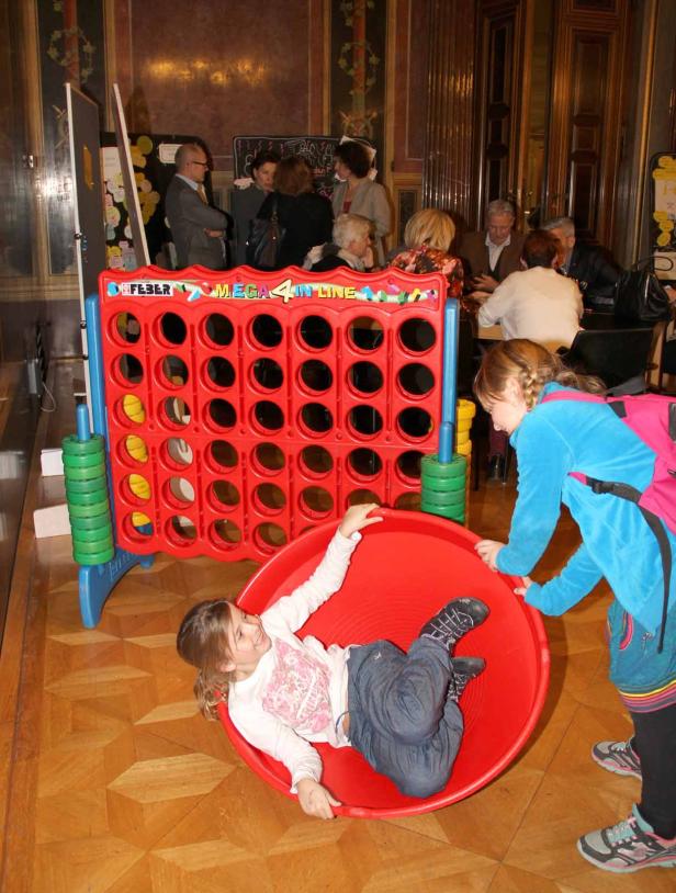 Ein Mädchen liegt in einem roten Spielzeugtunnel, während ein anderes Mädchen daneben steht.