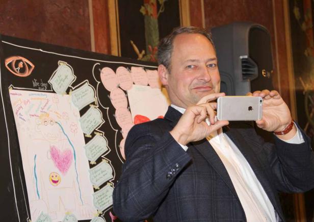 Ein Mann im Anzug fotografiert ein Plakat mit einer Zeichnung und Notizen.