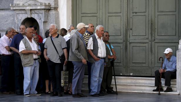 Eine Gruppe älterer Männer wartet vor einem Gebäude, ein Mann sitzt auf den Stufen.