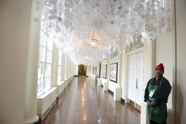 Ein Mann steht in einem mit Schneeflocken geschmückten Flur mit einem Weihnachtsbaum im Hintergrund.