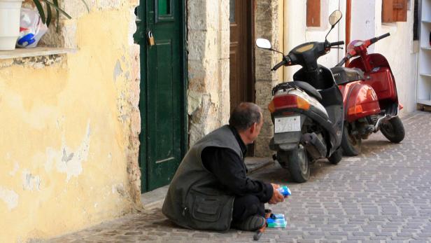 Ein Mann hockt auf einer Gasse neben zwei geparkten Motorrollern.