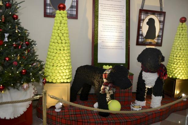 Weihnachtsdekoration mit Tennisball-Bäumen und Stofftier-Hunden auf einer karierten Plattform.