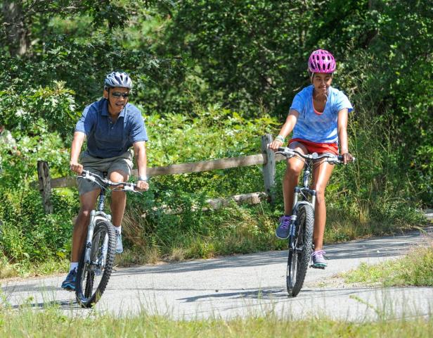 Barack Obama und Malia Obama fahren mit Fahrrädern auf einem Weg.