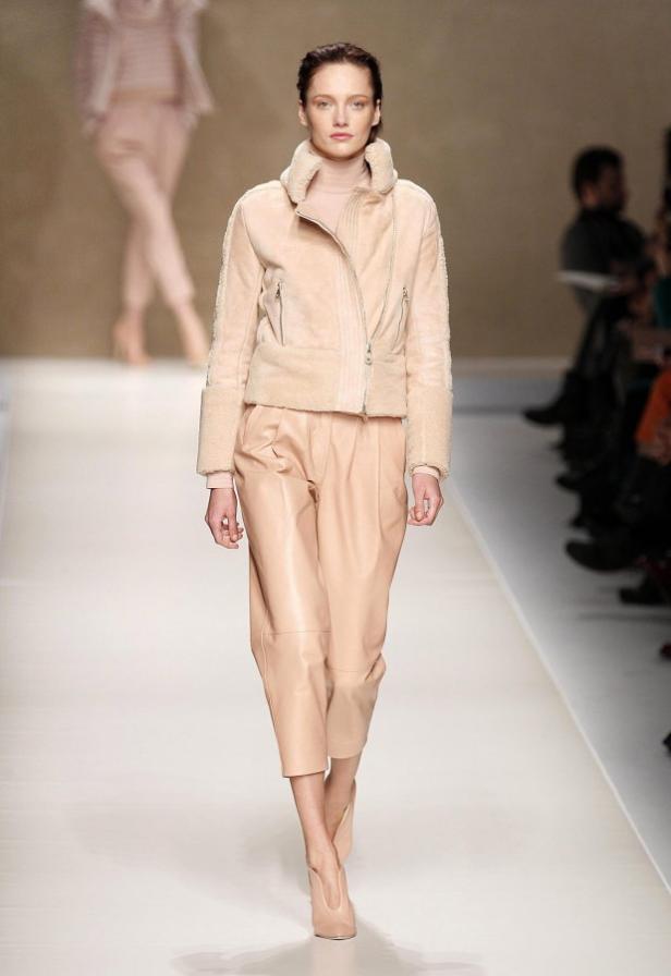 Eine Frau in einer hellrosa Jacke und Hose auf einem Laufsteg.