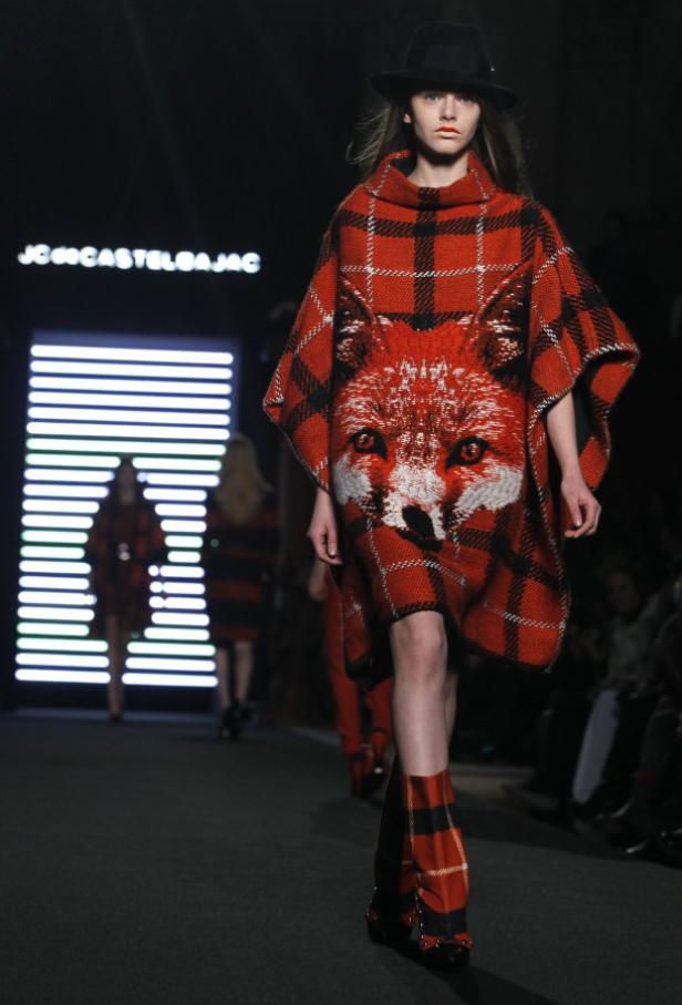 Ein Model auf dem Laufsteg trägt einen roten Poncho mit einem Fuchsmotiv.
