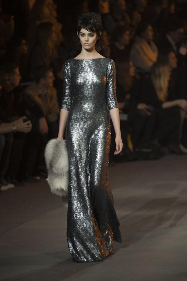 Ein Model präsentiert ein silbernes Paillettenkleid mit Pelzakzent auf dem Laufsteg.