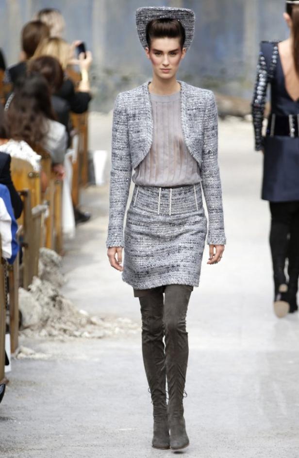 Eine Frau in einem grauen Tweed-Kostüm und Overknee-Stiefeln auf einem Laufsteg.