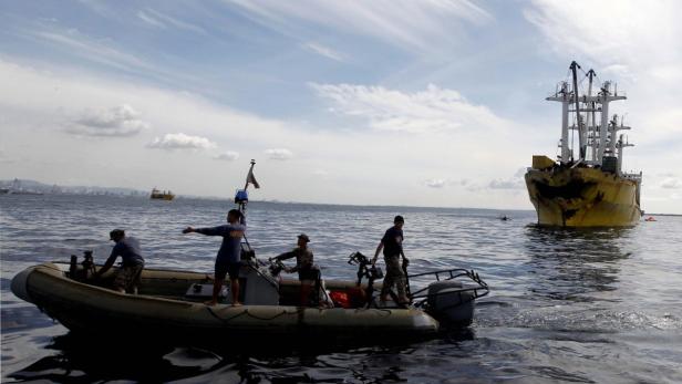 Ein kleines Boot mit vier Personen nähert sich einem großen, gelben Schiff.