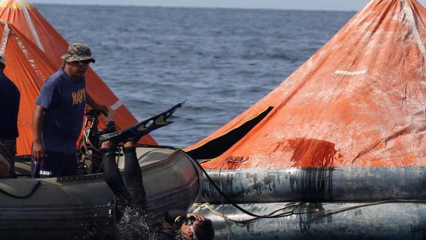 Ein Taucher steigt von einem Schlauchboot ins Wasser, während ein Mann im Hintergrund zusieht.