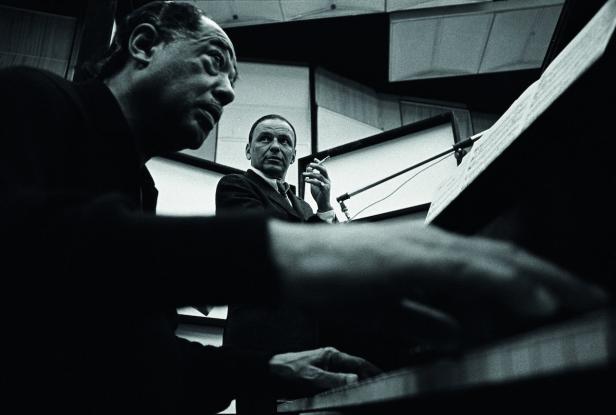Duke Ellington spielt Klavier, während Frank Sinatra im Hintergrund eine Zigarette raucht.