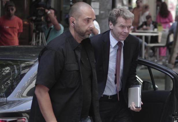 Ein Mann im Anzug steigt aus einem Auto, begleitet von einem Sicherheitsmann.