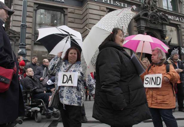 Menschen demonstrieren mit Schildern „Da sind“ und Regenschirmen in einer Stadt.