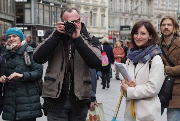 Ein Fotograf macht ein Foto von einer Frau mit einem Schal in einer belebten Stadt.
