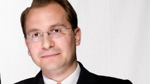 Paul Pöltner Ein Mann mit Brille, Anzug und Krawatte vor einem weißen Hintergrund.