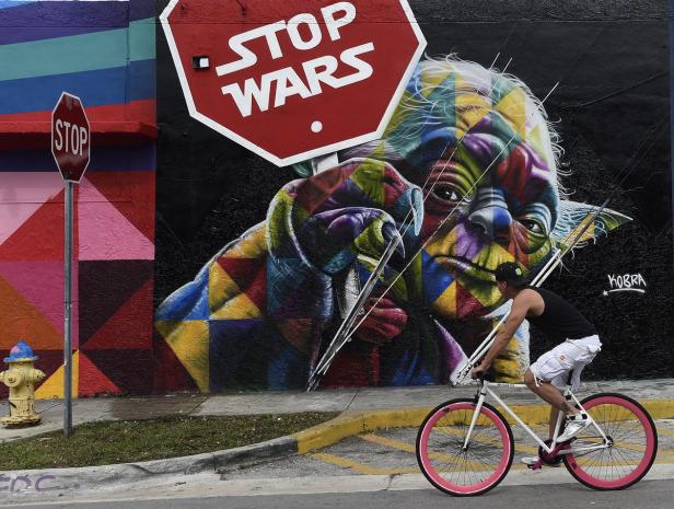 Ein Mann fährt mit dem Fahrrad an einem Wandbild von Yoda und einem „Stop Wars“-Schild vorbei.