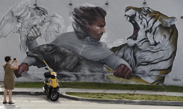 Eine Frau fotografiert ein Wandgemälde mit einem Mann, einem Tiger, einem Wolf und einer Eule.