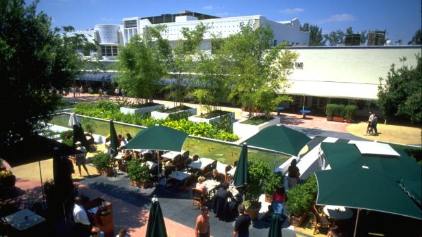 Ein Außenbereich mit Tischen und Sonnenschirmen neben einem Wasserbecken.