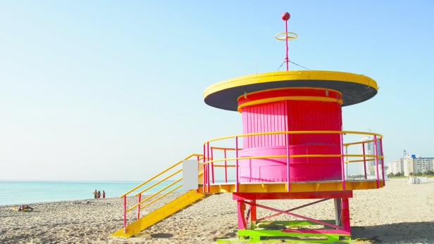 Ein farbenfroher Rettungsschwimmerturm steht an einem sonnigen Strand.