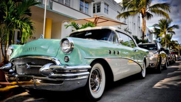 Ein mintgrüner Buick parkt auf einer Straße mit Palmen in Miami Beach.