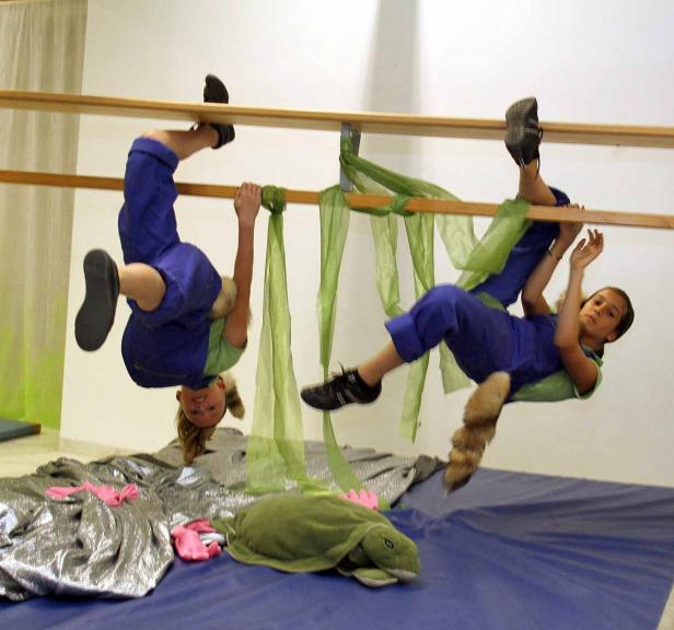 Zwei Kinder in Kostümen hängen an einer Reckstange in einem Raum.