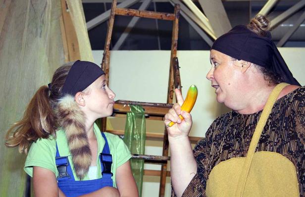 Eine Frau mit Kopftuch hält eine gelbe Zucchini und spricht mit einem Mädchen.