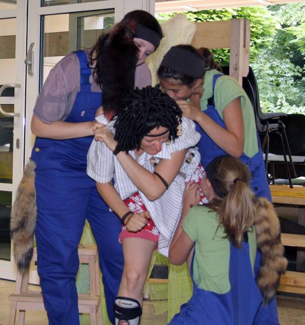 Vier Personen in blauen Overalls scheinen eine Person mit Dreadlocks zu unterstützen.